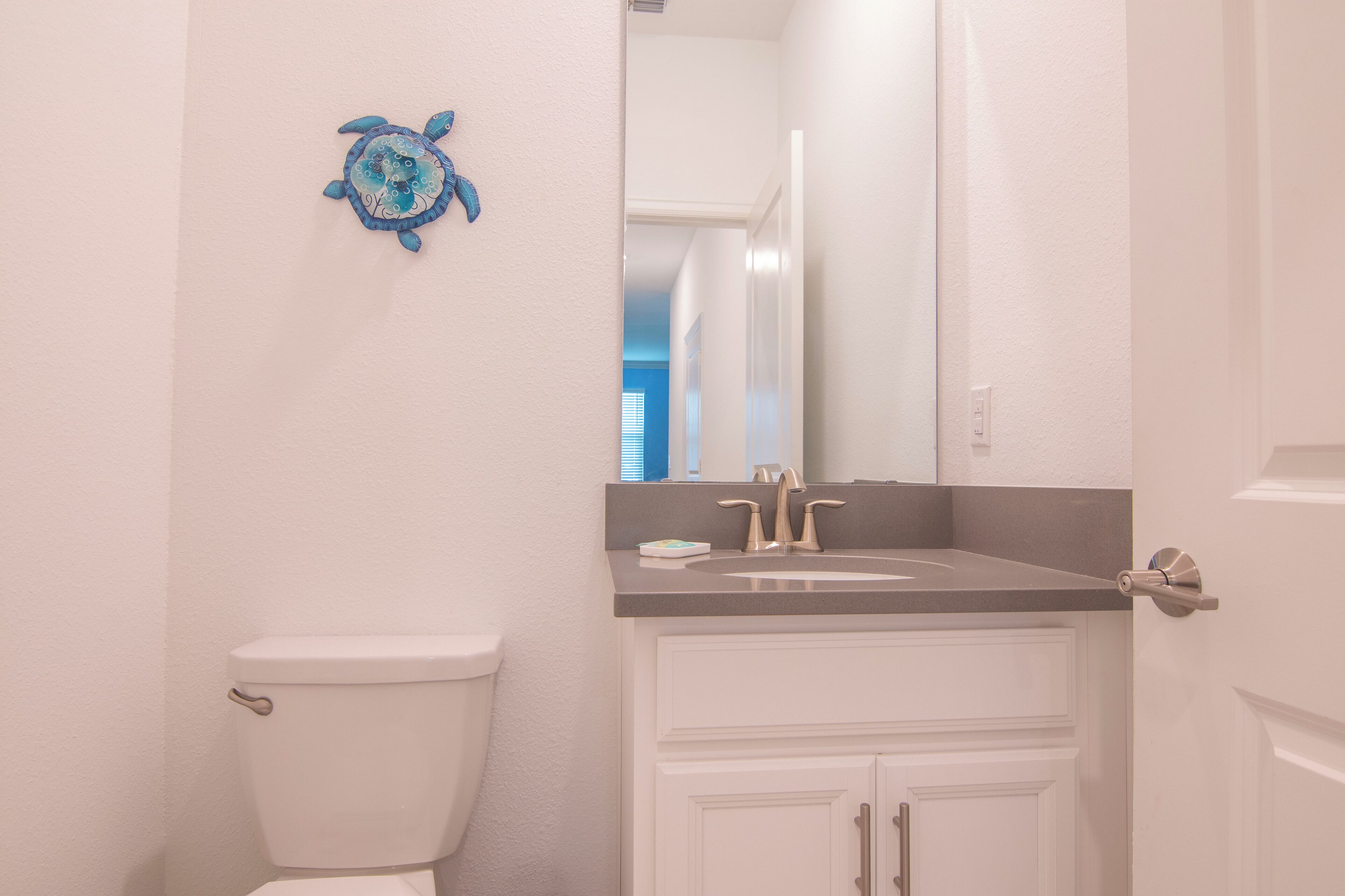 A bathroom with a white toilet, a sink with a mirror above it, and a decorative blue turtle on the wall.