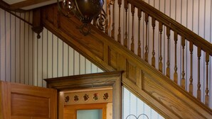 Uma escada de madeira com corrimão decorativo leva a um patamar no segundo andar. Uma porta de madeira com uma placa de boas-vindas em formato de coração é visível à esquerda.