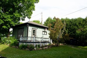 A small, single-story house with a porch, surrounded by a garden and trees.