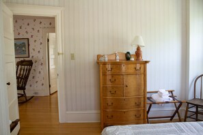 A bedroom with a wooden dresser, a chair, a bed, and a lamp.