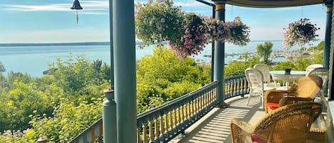 Un espacio al aire libre cubierto con mobiliario de mimbre, cestas de flores colgantes y vistas al agua.