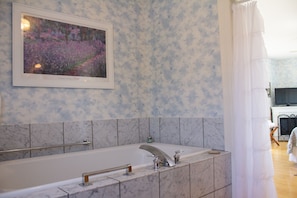 A bathroom with a marble tub, a framed painting above it, and a shower curtain. - Harbor Hill House Bayfield, WI (Bayfield)