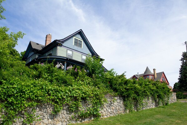 A house with a stone wall and greenery in front.