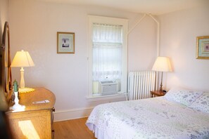 A bedroom with a bed, two bedside lamps, a dresser, a window with blinds, and a radiator. - Harbor Hill House Bayfield, WI (Bayfield)