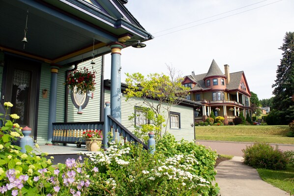 A two-story house with a porch, a front yard with flowers, and a driveway.