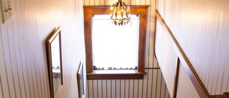 Una escalera de madera con un candelabro, una ventana y un cuadro en la pared.