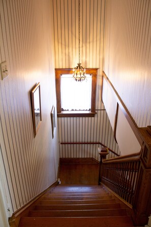 A wooden staircase with a chandelier, a window, and a picture frame on the wall.