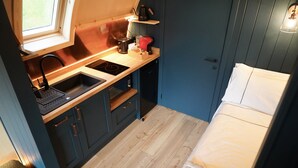 A compact kitchenette with a sink, stove, and storage cabinets. - Luxury Rural Cabin with Wood Fired Hot Tub (Canonbie)