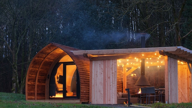 A cozy, semi-open wooden structure with a curved roof, a visible interior with a fireplace, and string lights. - Luxury Rural Cabin with Wood Fired Hot Tub (Canonbie)