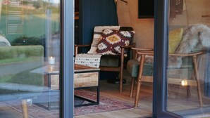 A cozy interior with a glass door leading to a small seating area with a chair and a sofa, a wooden coffee table, and a rug. - Luxury Rural Cabin with Wood Fired Hot Tub (Canonbie)