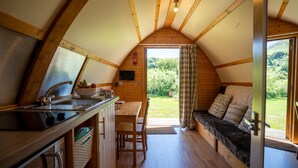 A cozy cabin interior with a wooden interior, a kitchen area with a sink and counter, a dining table, and a seating area with a bench and cushions. - Cosy Rural Cabin With Hot Tub (Pwllheli)