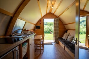 A cozy cabin interior with a wooden interior, a kitchen area with a sink and counter, a dining table, and a seating area with a bench and cushions.