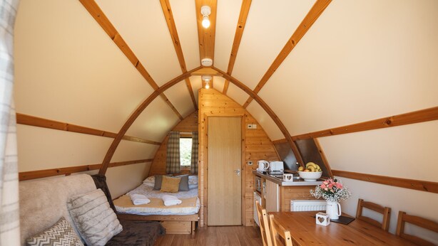 A cozy attic bedroom with a wooden ceiling, a bed with pillows, a small kitchenette, and a dining table. - Cosy Rural Cabin With Hot Tub (Pwllheli)