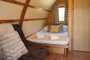 A cozy, wooden cabin bedroom with a loft bed, a fluffy chair, and a plaid curtain.