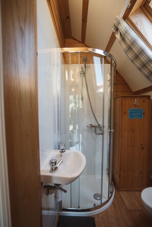 A glass-enclosed shower with a sink, wooden beams, and a wooden door with a plaque.