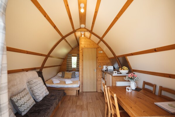 A cozy attic bedroom with a wooden ceiling, a bed with pillows, a small kitchenette, and a dining table.