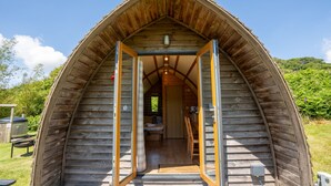Una cabana de fusta amb teulada a dos vessants, on es veu l'interior amb un llit i una cuina americana petita, i una porta d'entrada a la cabana.