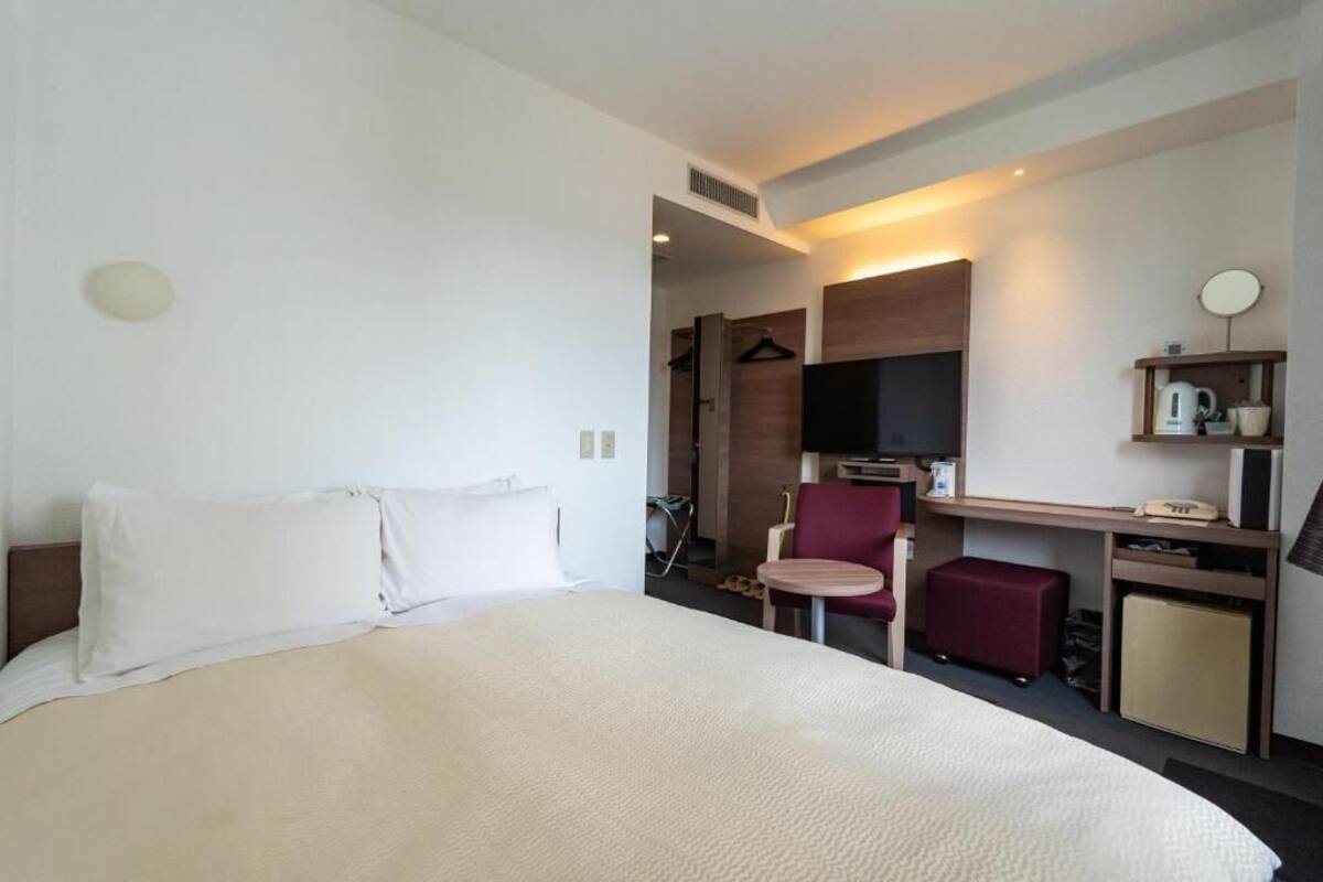 A hotel room with a large bed, a desk with a chair, a television, and a small cabinet.