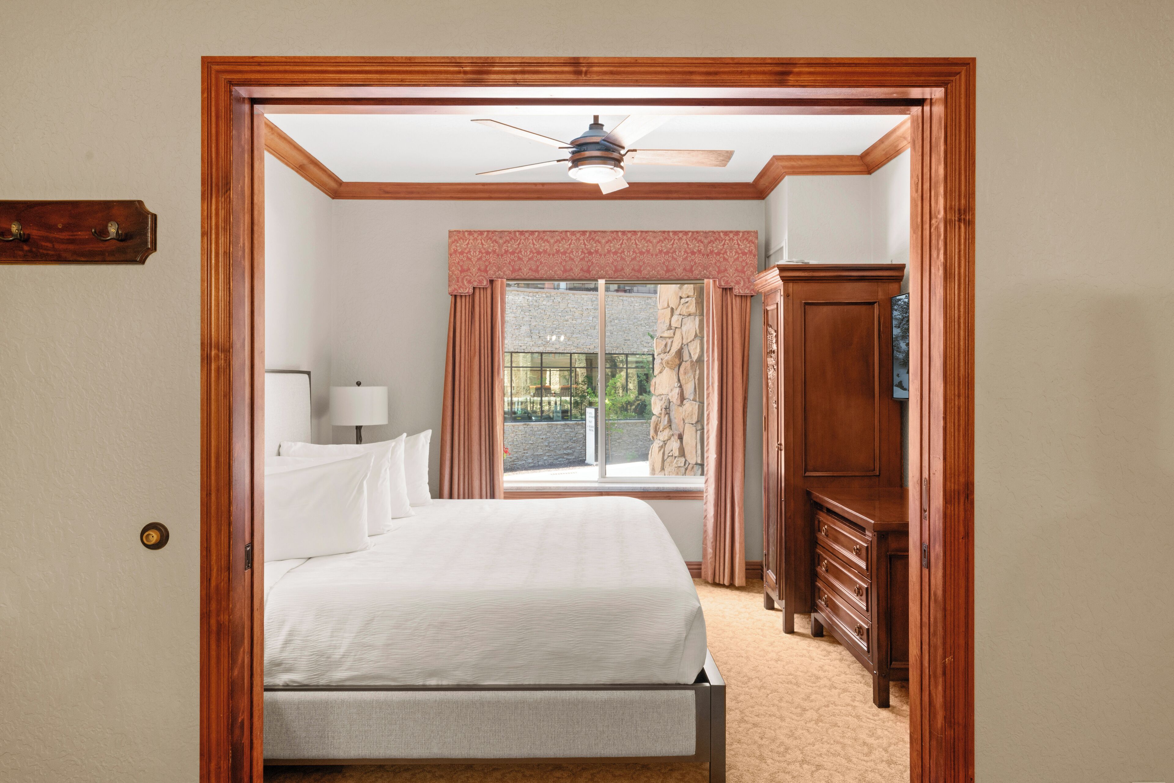 A bedroom with a bed, a dresser, a window with curtains, and a ceiling fan.