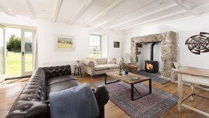 A cozy living room with a stone fireplace, a leather sofa, and a dining area. - Worvas Counthouse -  Country Cottage - Hot Tub - Pet Friendly (St Ives)