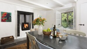 A dining area with a fireplace, a table set with a vase of flowers, a bowl of apples, and a bottle of wine. - Worvas Counthouse -  Country Cottage - Hot Tub - Pet Friendly (St Ives)