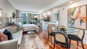 A modern living room with a sofa, a glass dining table, and a view of a cityscape through large windows. - Coconut Grove Studio: Sleeps 4 Includes Parking (Miami)