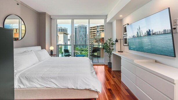 A modern bedroom with a large bed, a TV mounted on the wall, and a balcony with a city view. - Coconut Grove Studio: Sleeps 4 Includes Parking (Miami)