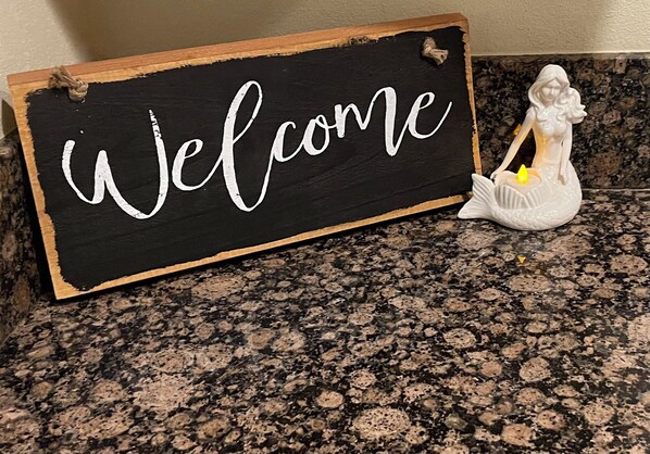 A welcome sign with a mermaid figurine on a granite countertop.