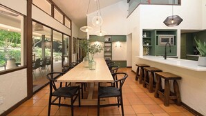 A modern kitchen with a long wooden table, bar stools, and pendant lighting.