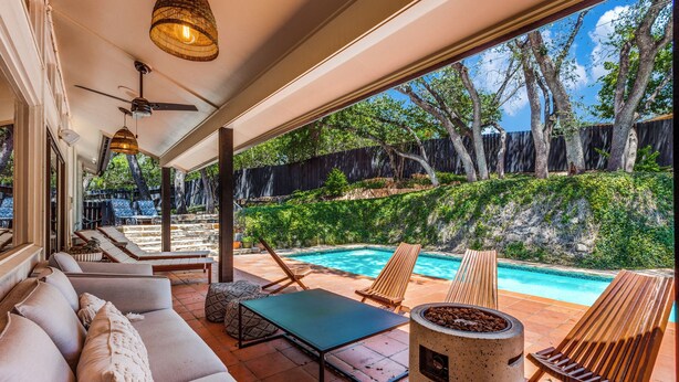 An outdoor patio with a pool, lounge chairs, a table, and a ceiling fan.