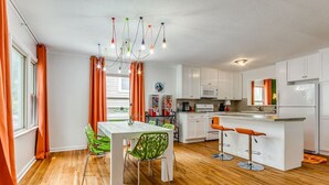 Une cuisine moderne avec des meubles blancs, un plancher en bois, un coin repas avec une table blanche et des chaises vertes, et un bar avec des tabourets orange.