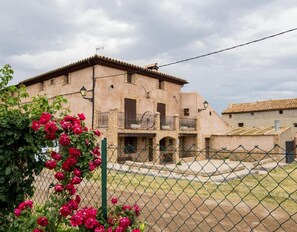 A traditional building with a balcony, a fence, and a garden with red flowers.