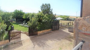 Un patio con vista a un campo cubierto de césped, una valla de madera y un muro de piedra.