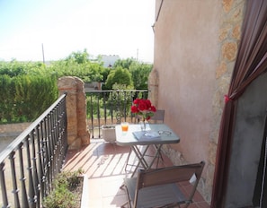A balcony with a table, chair, and a vase of red flowers.