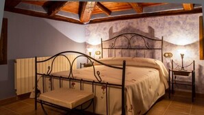 Un dormitorio con estructura de cama metálica, una mesita de noche, un banco y un radiador fijado a la pared.