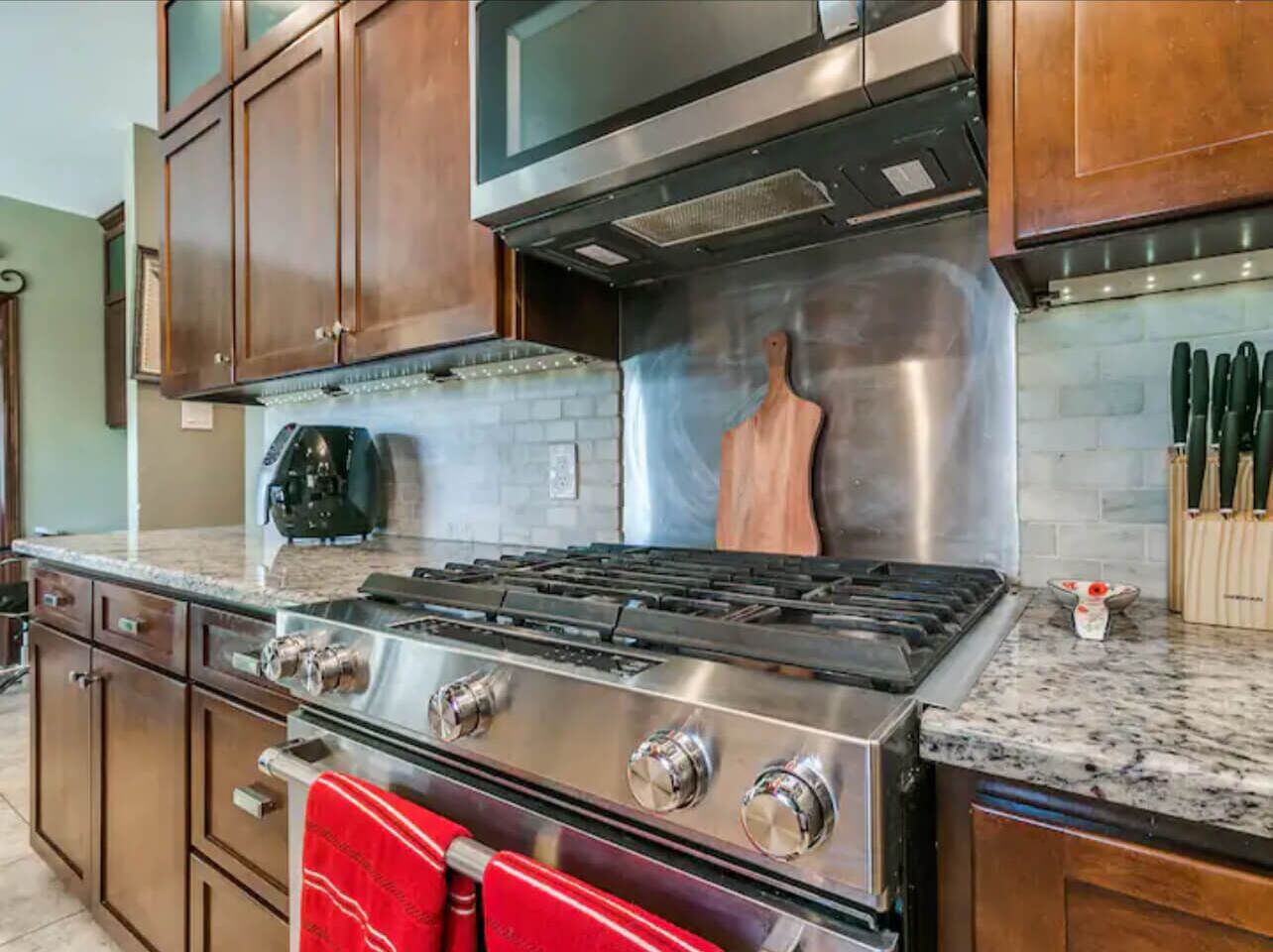 A kitchen with a stainless steel stove, wooden cabinets, and a microwave.