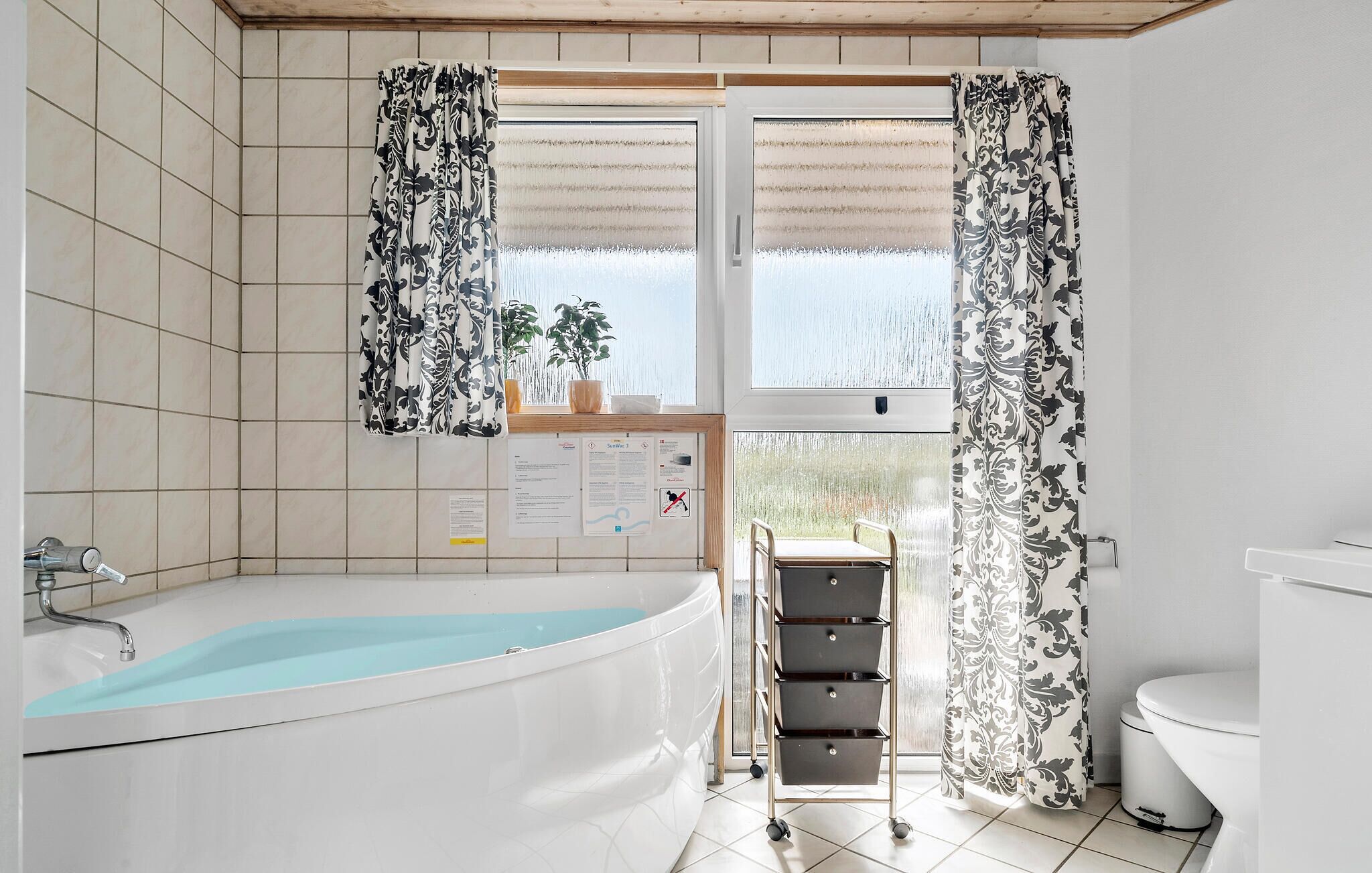 A bathroom with a bathtub, toilet, and a window with curtains.