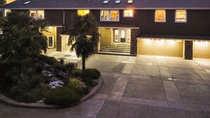A two-story building with a garage, a covered driveway, and a landscaped front yard with palm trees and shrubs.