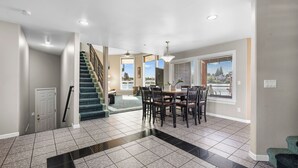 A spacious living area with a dining table and chairs, a staircase, and a view of the outdoors.