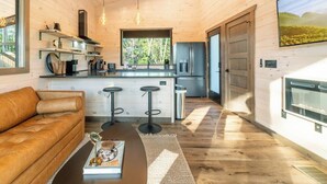 A modern log cabin interior with a living area, kitchen, and bar stools. - New Modern Design! Treetop Escape! Hot Tub, Fireplace, Fire Pit & Views!! (Sevierville)