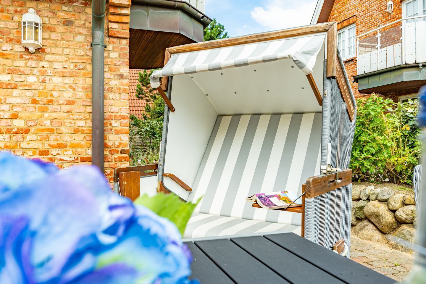 A covered outdoor seating area with a striped awning, a wooden bench, and a table with a book.
