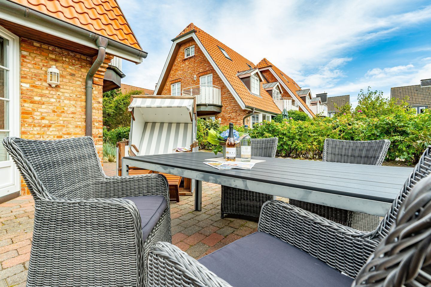 An outdoor patio with wicker furniture and a table, surrounded by brick buildings and greenery.