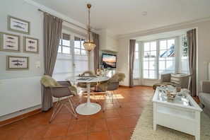 Una sala de estar bien iluminada con comedor, ventanas amplias y televisor.