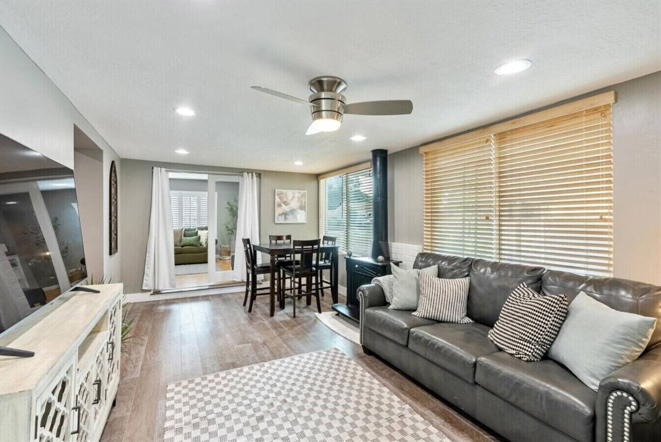A modern living room with a leather sofa, a dining table, and a ceiling fan.
