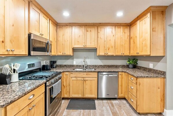 A kitchen with wooden cabinets, granite countertops, stainless steel appliances, and a dishwasher.