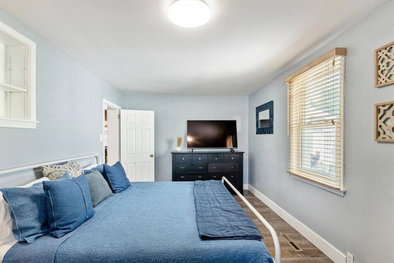 A bedroom with a bed, dresser, TV, and window blinds.
