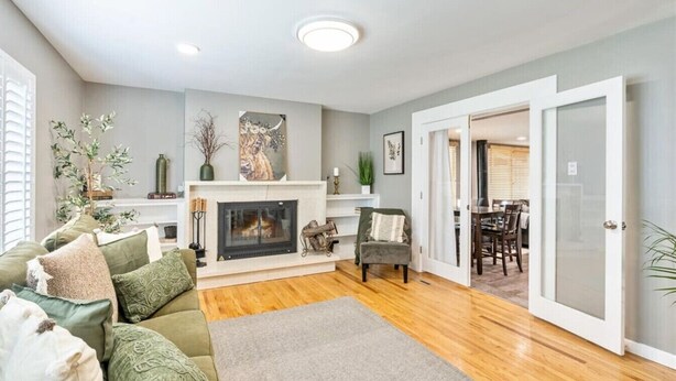 A living room with a fireplace, a green sofa, and a dining area visible through an open door.