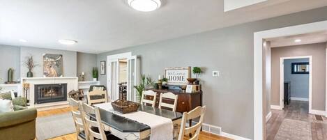 A modern living room with a fireplace, dining area, and a hallway leading to another room.