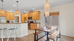 Una cocina moderna con armarios de madera, una isla central, taburetes de bar e iluminación colgante.