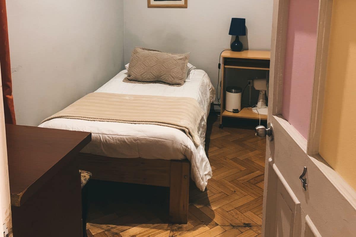 A small, neatly arranged bedroom with a single bed, a bedside table, and a nightstand.